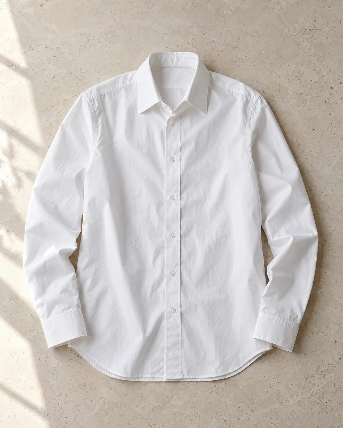 A white cotton poplin shirt laid flat on limestone