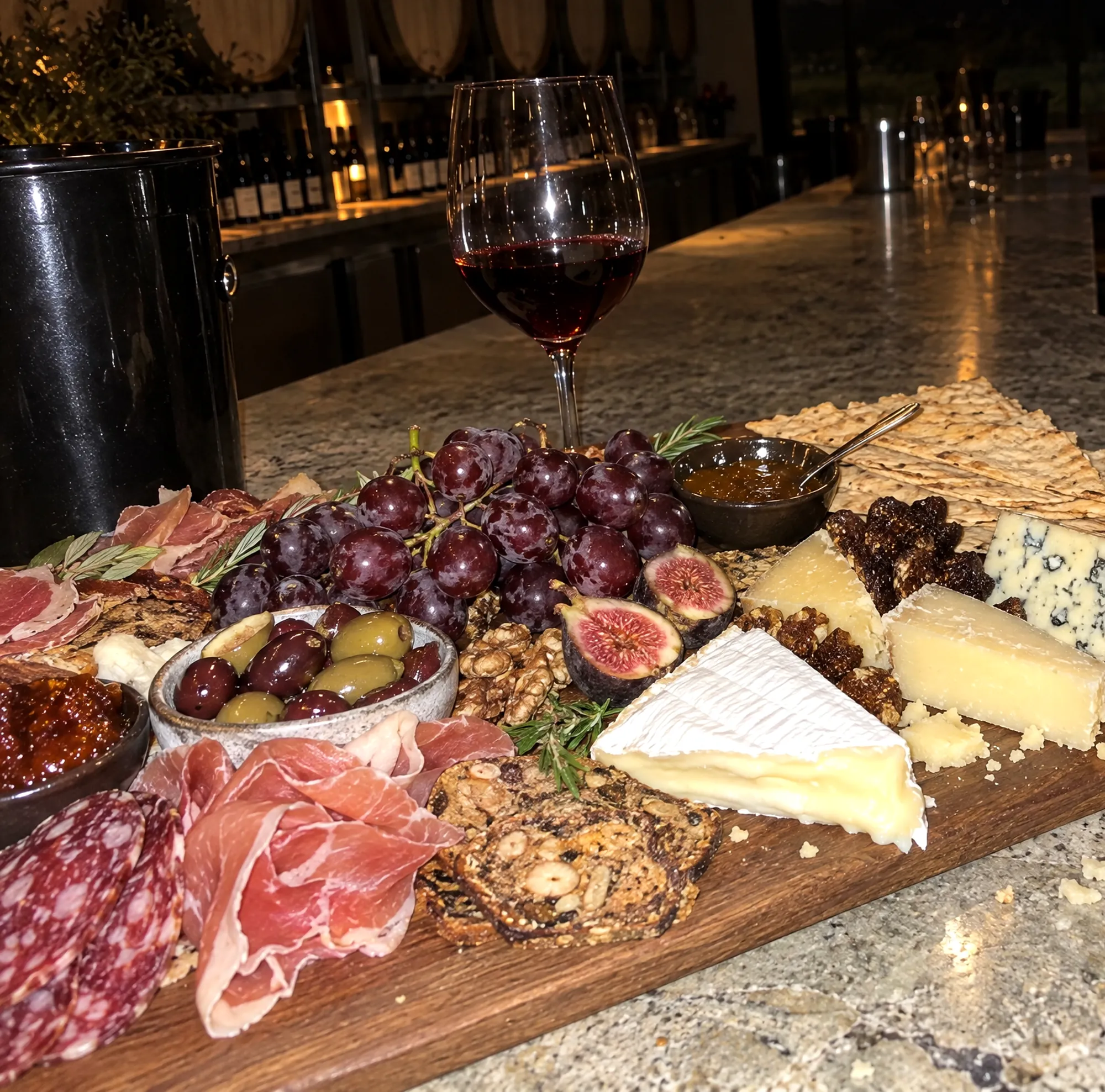 A grazing board of cured meats, cheeses, figs, grapes and crackers beside two glasses of red wine
